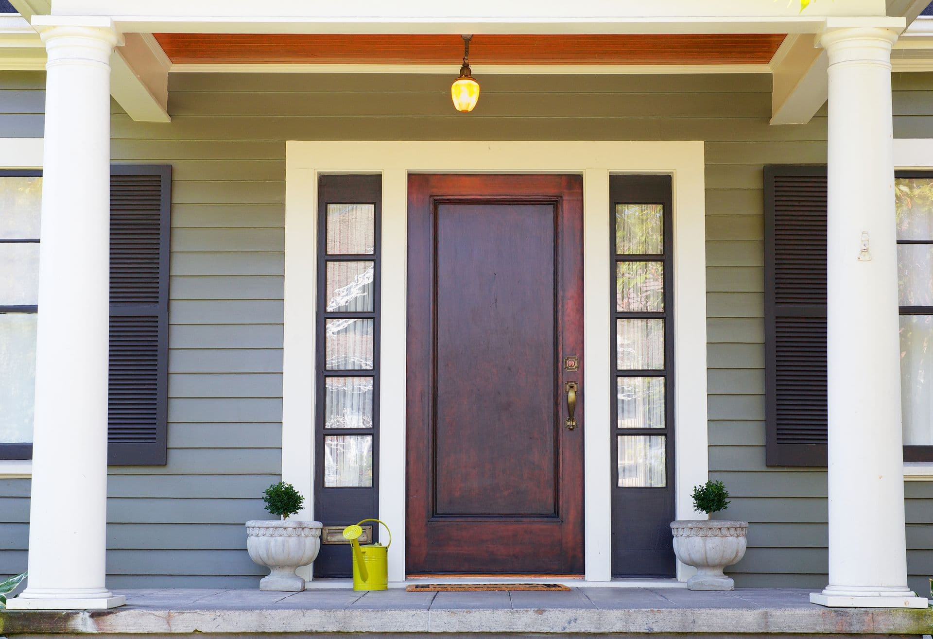 Brown stained Front Door on a home with bordering window and a pillared porch